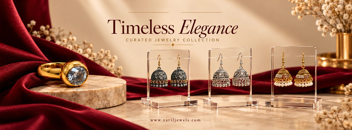 Zarif Jewels Pakistan artificial jewellery collection featuring gold-tone crystal fashion ring and traditional black, silver and gold jhumka earrings on burgundy velvet. Artificial Jhumka Earrings & Fashion Rings Online in Pakistan | Zarif Jewels.